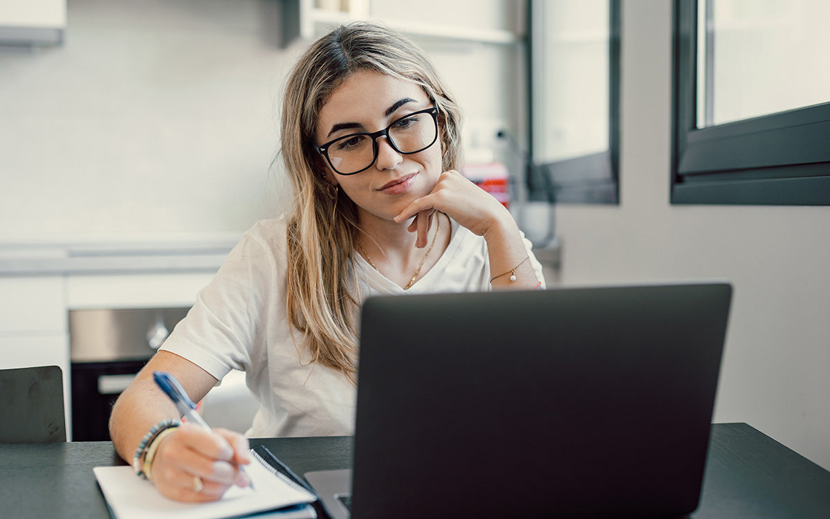Blonde Frau mit Brille schreibt bei einem Online-Vortrag mit