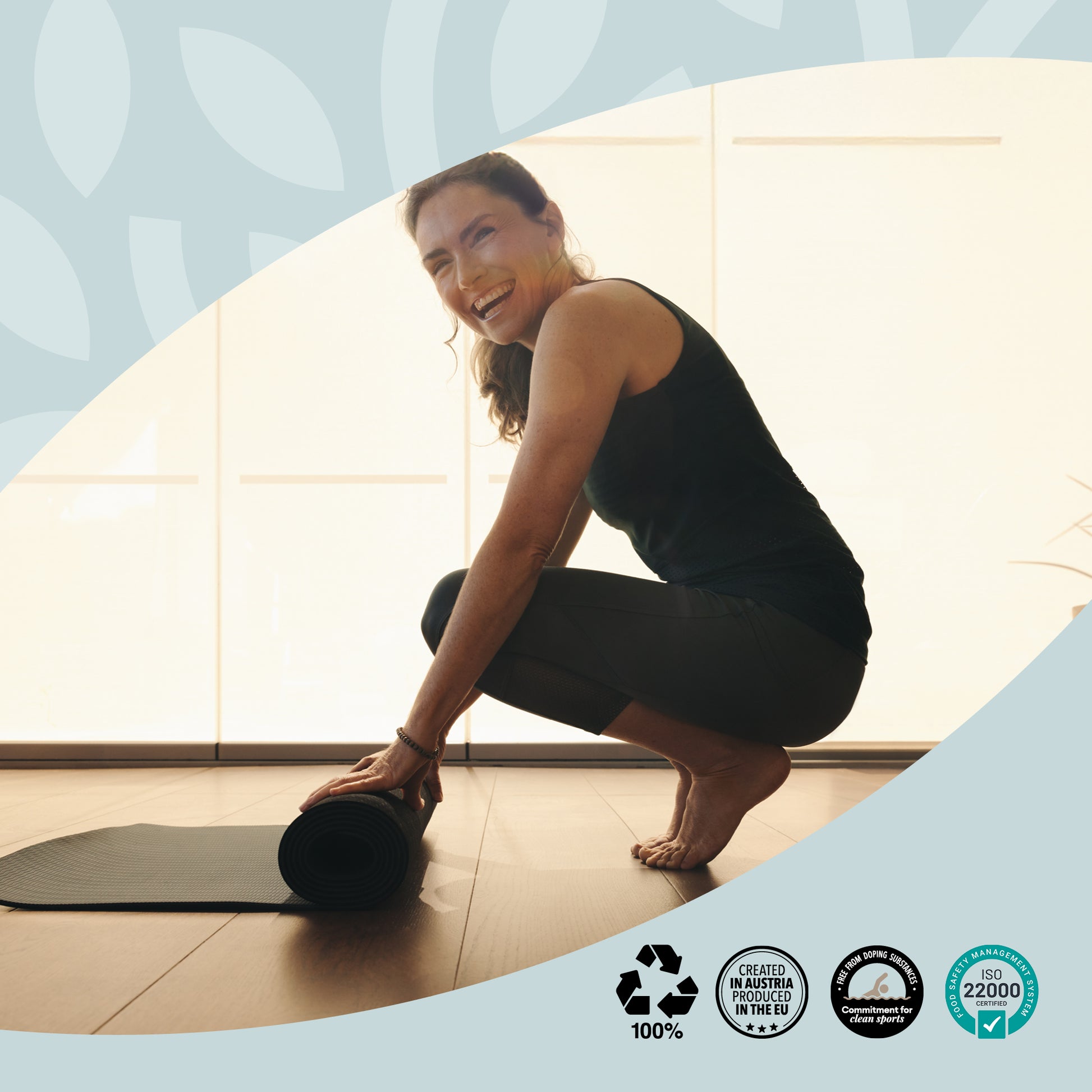 Eine Frau in Sportkleidung lacht beim Aufrollen ihrer Yogamatte in einem hellen Raum. Symbol für Vitalität, Bewegung und Wohlbefinden mit vabon. Unten Nachhaltigkeitssiegel: Recycling, Created in Austria, CO2-kompensiert, ISO 22000 zertifiziert.