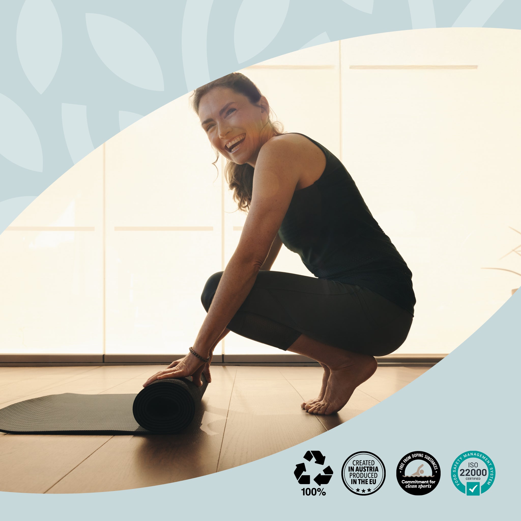 Eine Frau in Sportkleidung lacht beim Aufrollen ihrer Yogamatte in einem hellen Raum. Symbol für Vitalität, Bewegung und Wohlbefinden mit vabon. Unten Nachhaltigkeitssiegel: Recycling, Created in Austria, CO2-kompensiert, ISO 22000 zertifiziert.