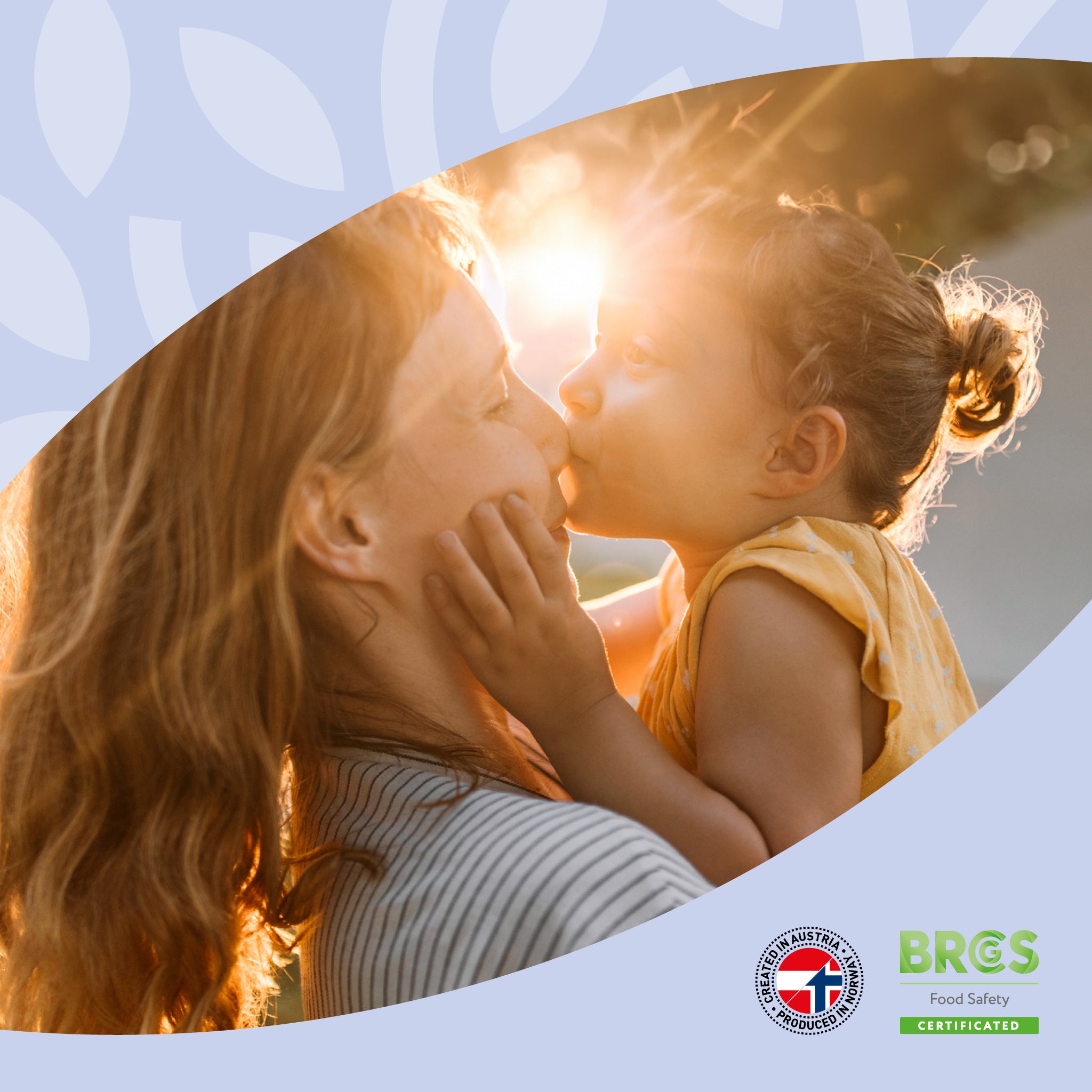 Eine erwachsene Person hält ein Kind im Arm, beide küssen sich im Sonnenlicht. Symbol für Vertrauen, Geborgenheit und Wohlbefinden mit vabon. Unten Nachhaltigkeitssiegel: Created in Austria und BRCGS Food Safety Zertifizierung.