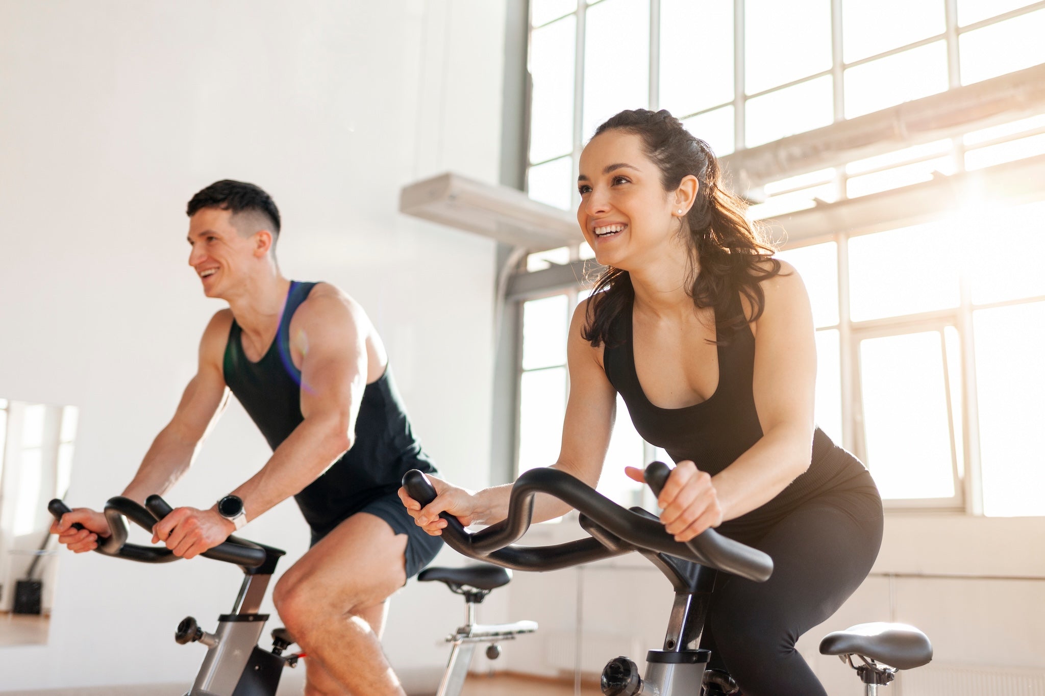 Frau und Mann trainieren lachend auf Spinning-Bikes im Fitnessstudio – Indoor-Cycling für Ausdauer, Gesundheit und Energie.