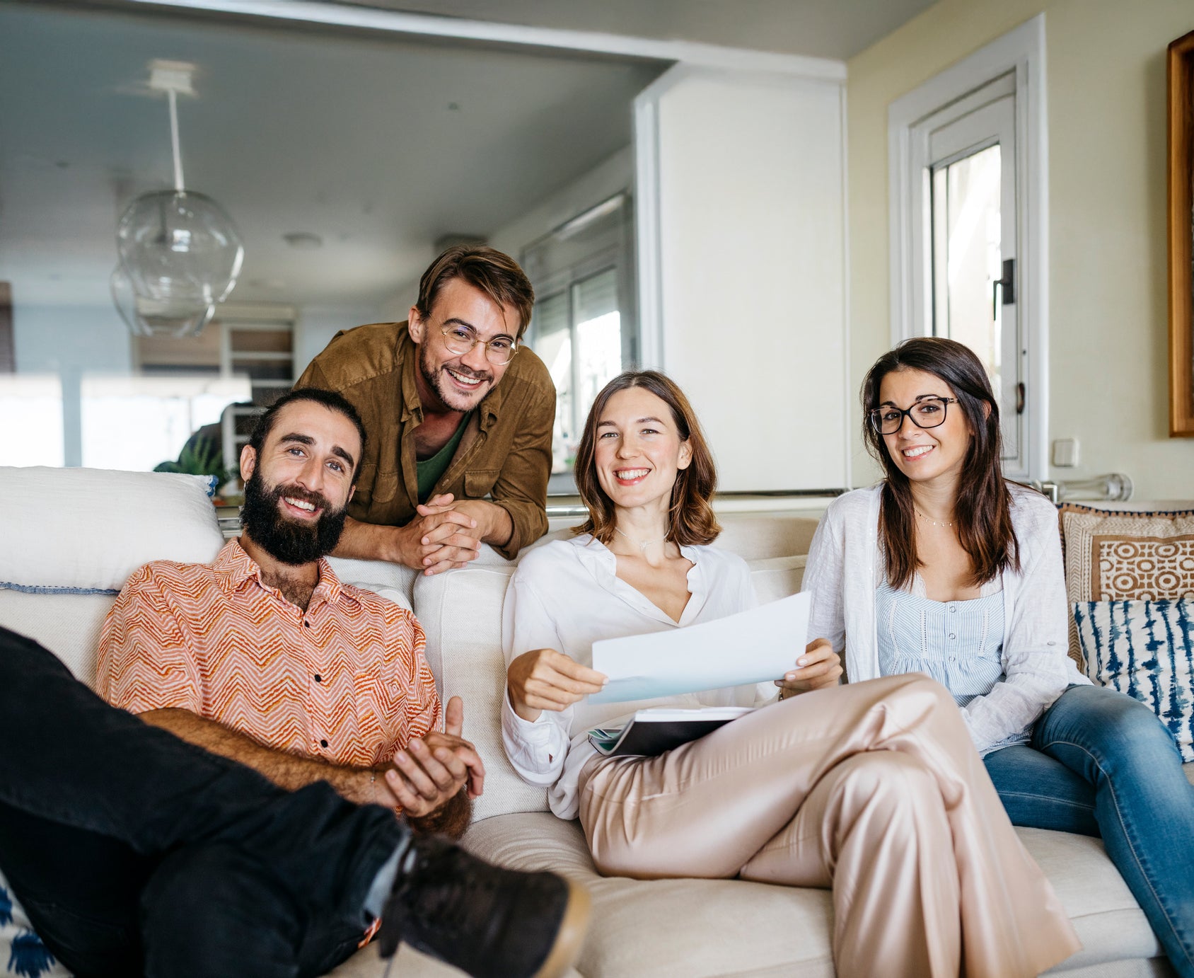 Vier Personen sitzen entspannt in einem hellen Wohnzimmer, lachen und schauen in die Kamera. Symbol für Gemeinschaft, Vertrauen und Lebensfreude mit vabon